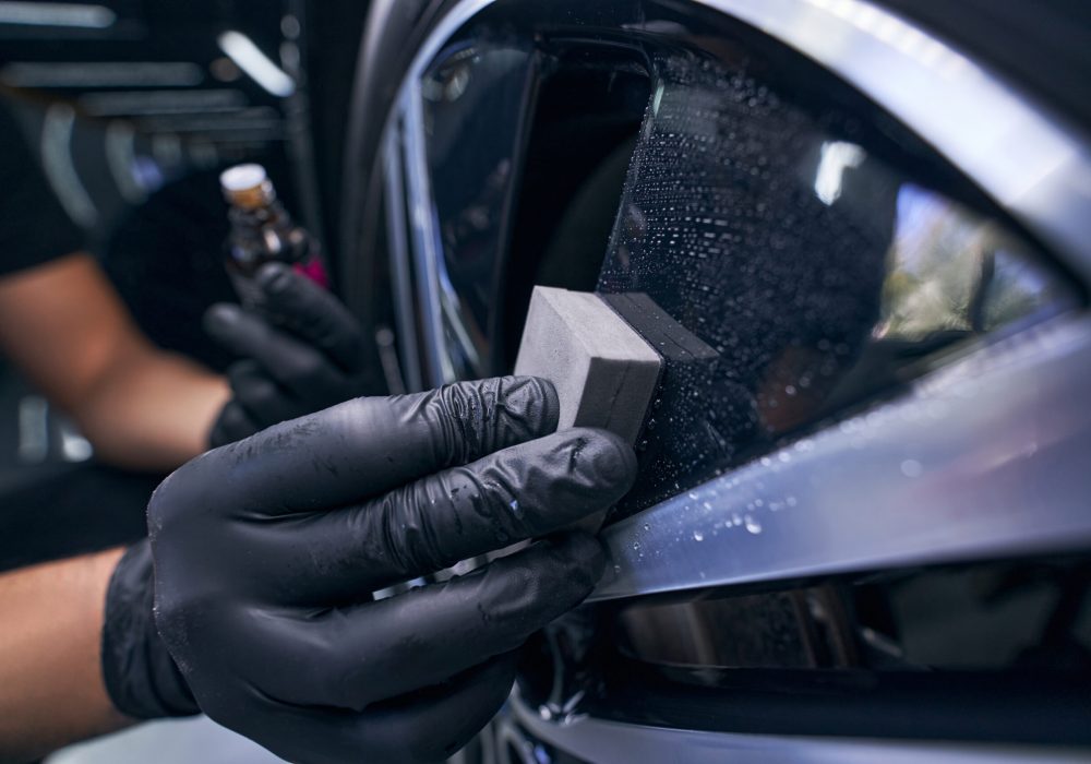 Worker in gloves waxing the car wheel tire closeup. Automobile care and detailing auto service