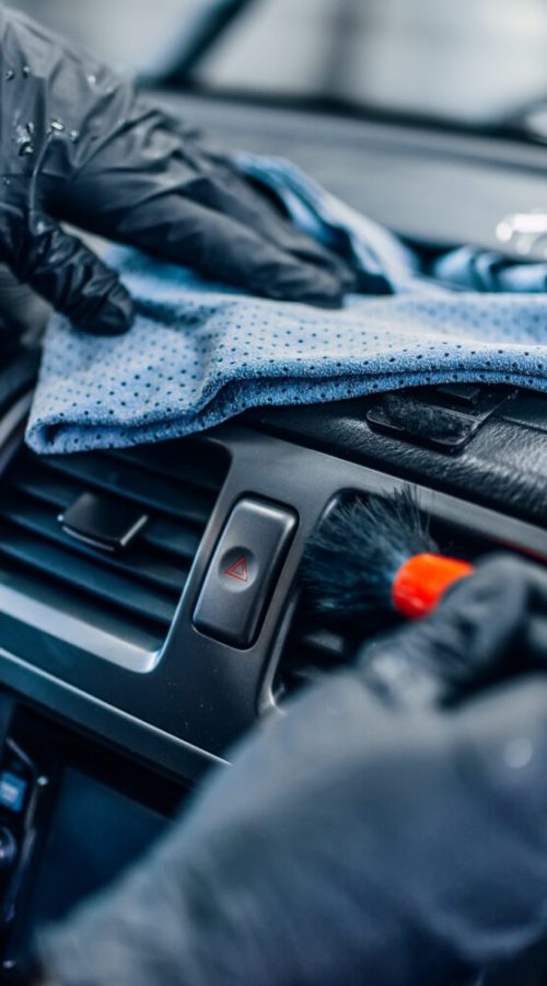 Auto detailing of car interior on carwash service. Worker in gloves cleans salon with brush