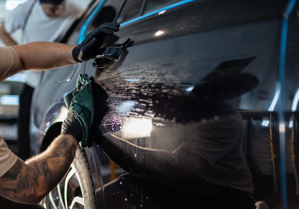 Man car washer washes car and wipes black car with rag in detailing studio